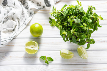 Creative flat lay overhead of fresh organic green mint and aromatic limes on white wooden table. Ingredients for  aromatic vitamin drink