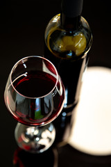 a glass of red wine with a bottle of wine in top view with a background in blurry black and a white light reflection