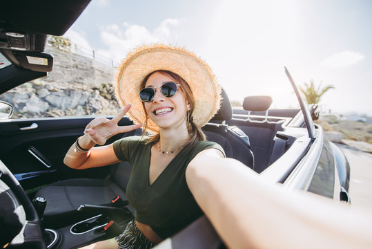 Happy young woman takes a selfie on a convertible car at vacation at summertime