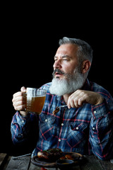 Brutal gray-haired adult man with a beard eats mustard steak and drinks beer, concept of a holiday, festival, Oktoberfest or St. Patrick's Day
