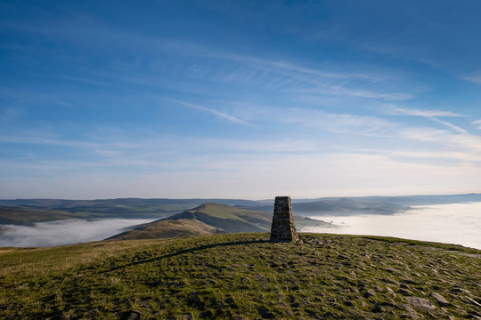 Trig point on top of Mam Tor, Peak District, UK. Early morning with mist in Edale and Hope Valley, and the Great Ridge rising above the mist