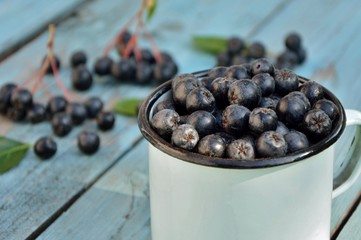 Black chokeberry berries in a mug on a blue wooden background close-up