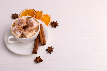 Cup of coffee with marshmallows and cocoa, leaves, dried oranges, spices, on a white background. Delicious hot autumn drink, morning mood. Copy space.