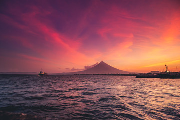 Naklejka na ściany i meble Great Mayon Volcano on Luzon Island Panoramic View. Oriental Mountain Peak and Beautiful Color Sky Sunset. Photography on Ocean with Ship Boat. Philippines Seaside Ecoregion Scenery