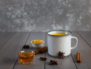 Obraz na płótnie Canvas Golden milk, turmeric, honey, ginger root, cinnamon and other ingredients on grey wooden background. This drink is useful for colds and to increase immunity. Masala Haldi Doodh.