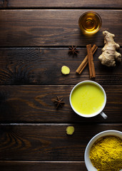 Golden milk and ingredients for its preparation: turmeric, ginger root, anise, honey, cinnamon on a dark wooden background. Masala Haldi Doodh.