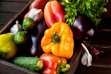 Autumn vegetables (pepper, eggplant, tomatoes, garlik, cucumbers) in a wooden box on a wooden table. The concept of healthy and diet food.