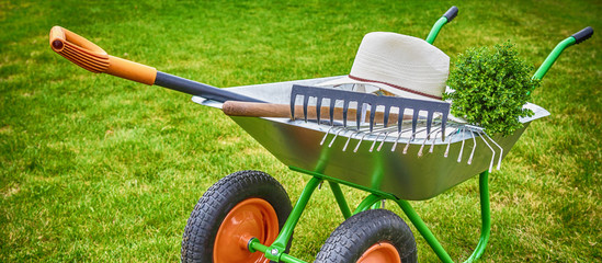 Wheelbarrow with Gardening tools in the garden.banner
