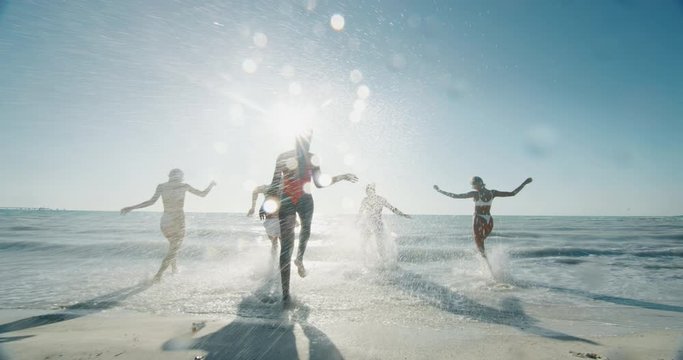Slow motion of young multi-ethnic carefree  friends in swimsuits are having fun and enjoying their summer vacation together on a beach with a sea in a sunny day.