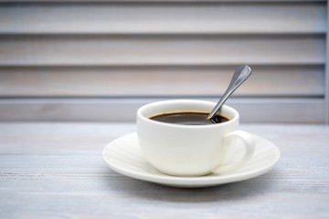 white ceramic coffee Cup with metal spoon on wooden background beautiful smoky color