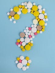 The concept of medicine and healthcare. Question mark made of pills of different colors on a blue background. Top view.