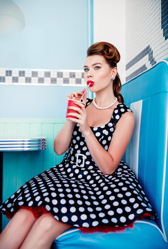 Retro (vintage) portrait of beautiful young girl sitting in cafe and drinking beverage. Pin up style portrait of young girl in dress