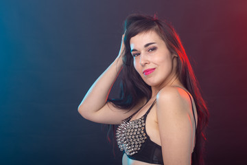 Attractive young sexy brunette woman in riveted top posing in the studio on a dark background. Concept of well-groomed young woman.
