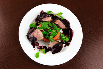 baked duck fillet in a sauce with herbs and berries in a plate
