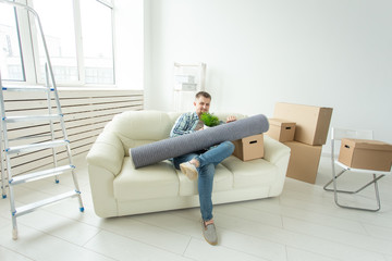 Positive young man sitting on the sofa with his things in the new living room after the move. Concept of housing affordability for young people.