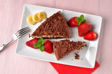 Homemade mole hole cake with whipped cream, banana, strawberries and fresh mint leaves on white decorative shaped plate. Pink place setting. Top view.