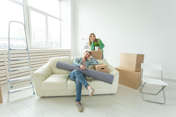 Satisfied cheerful young couple strong man and pretty woman holding their things in their hands sitting in the living room of a new apartment. Housewarming concept.