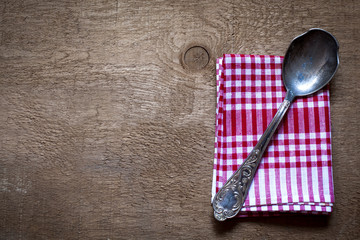 Checkered napkin with vintage silver spoon on wooden table background; top view, copy space,...