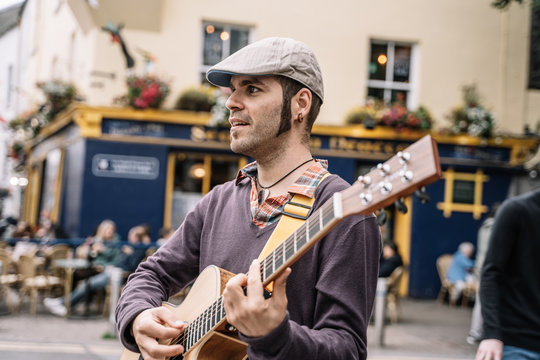 side view of a street performer playing the guitar - Powered by Adobe