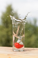 Ripe strawberries fell into a transparent glass of water and sprayed water around