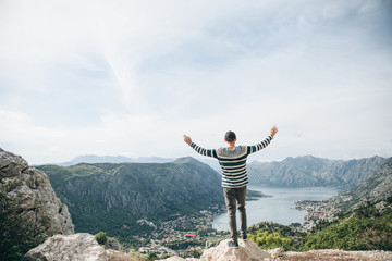 A guy or a tourist admires a beautiful view of the Bay of Kotor in Montenegro. He raised his hands up and shows how happy and free he is.