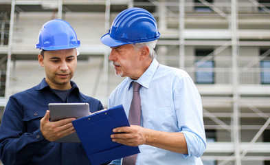 Two architect developers reviewing building plans at construction site using a tablet