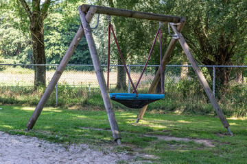 Children playground with a rope round swing with wooden poles surrounded by green vegetation, wonderful sunny summer day in south Limburg in the Netherlands, Holland