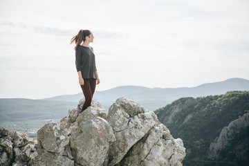 A girl in solitude stands on top of a mountain and she is happy.