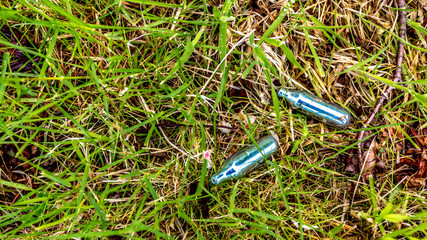 Empty bulbs of nitrous oxide or laughing gas on the grass in a public park, hippie crack is used as a recreational drug or as a party drug