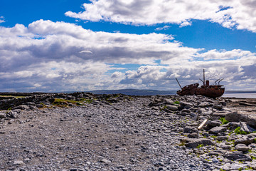 Fototapeta na wymiar View of a stone footpath on the island of Inis Oirr with the shipwreck of Plassey in the background, abandoned ship, old and rusty over time, wonderful sunny day in the Aran Islands, Ireland