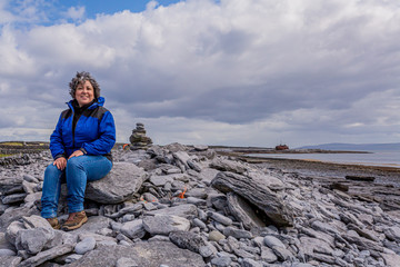 Happy and smiling Mexican woman sitting on the stones of the rocky beach of Inis Oirr Island with a...