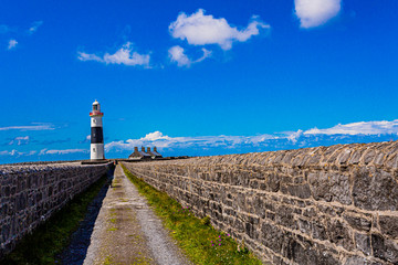 Straight rural road between limestone fences in the direction of the lighthouse in Inis Oirr island, wonderful sunny day with a blue sky in Inisheer, small island in the west of the coast of Ireland