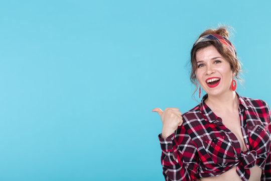 Positive beautiful young woman in a plaid vintage shirt looking at the camera and smiling posing on a blue background with copyspace
