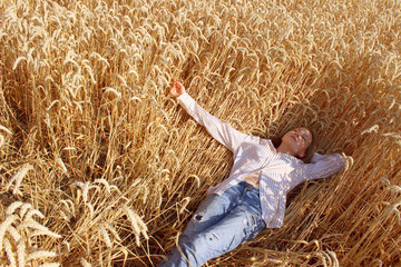 Full length shot of a pretty teenage girl enjoying the outdoors. Caucasian girl wearing a blue jeans and white shirt lying in wheat field. People, travel, freedom concept.