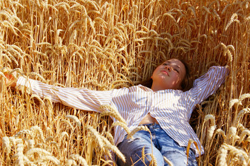 Full length shot of a pretty teenage girl enjoying the outdoors. Caucasian girl wearing a blue jeans and white shirt lying in wheat field. People, travel, freedom concept.