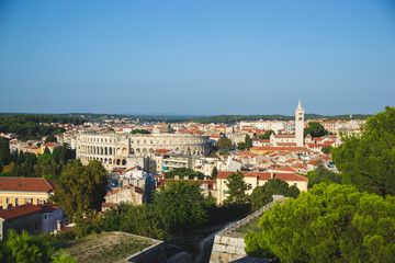 Fototapeta na wymiar Panoramic view of Pula Croatia with all buildings and green trees. Istria territory with brown roofs and mountains on the horizon. Amphitheater view, as travel postcard. Tourism wallpaper in Europe. 