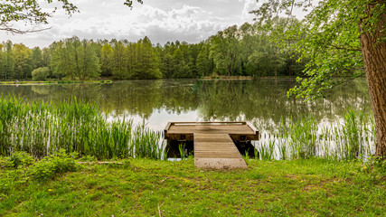 Fishing platform on the lake in the middle of the forest surrounded by trees and green vegetation with an impressive mirror lake, wonderful day to enjoy nature in the Netherlands Holland