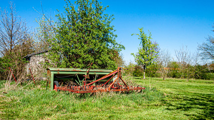 Fototapeta na wymiar Old, rusty and abandoned agricultural machinery, agricultural cultivator, kongskilde triltand grower, sunny spring day at the fruit farm in Oensel south Limburg in the Netherlands