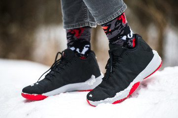 Male legs in athletic shoes, cropped jeans and fashionable socks standing on snow.  Stylish and trendy winter look.