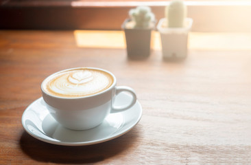 Hot coffee cup with latte art on the wooden table in the morning with sun shines through window.