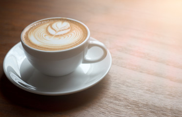 Hot coffee cup with latte art on the wooden table in the morning with sun shines through window.