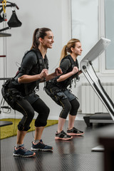 Two fit women in EMS suits doing squatting exercise