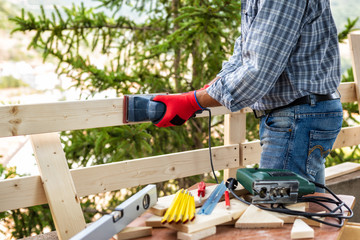 Adult carpenter craftsman with electric sander smoothes the boards of a wooden fence. Housework do it yourself. Stock photography.