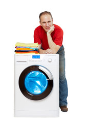 happy man smiling standing next to a new washing machine and a stack of clean laundry