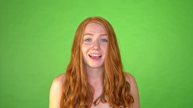 Slow motion portrait young red haired girl laughing into her hands green screen