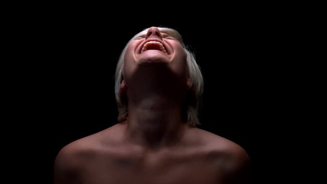 Young blond emotional naked woman screaming in the air. Slow motion shot with black background.