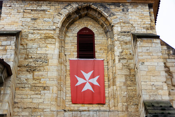 Tower window of an old building with the flag of the Order of Malta