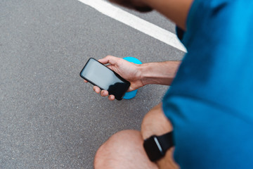 cropped view of sportsman with smartwatch holding smartphone with blank screen on running track