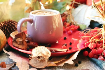 A cup of hot drink, berries, pumpkins, spices, a scarf, autumn leaves on the background of the window, the concept of home comfort, healthy food, tea for the common cold
