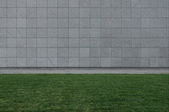 Building exterior detail. Outdoor summer shot of gray panels tiles for facades. Abstract urban background with tiled wall of shopping mall or supermarket. Green grass or lawn. Horizontal iamge